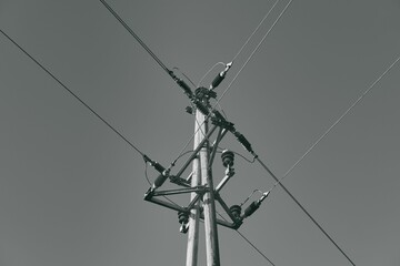 Low-angle closeup of a power pole with connected powerlines in greyscale