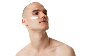 Handsome shitless young man with moisturizing cream on spotless face isolated on white studio...