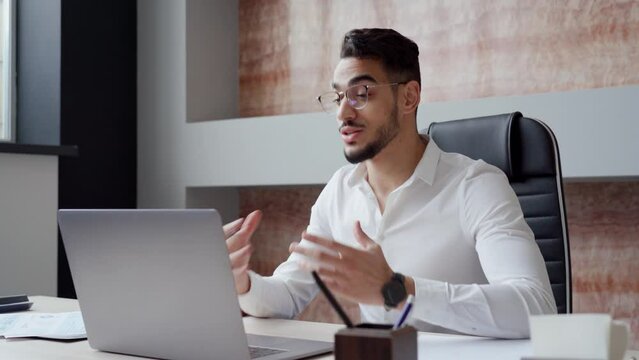 Busy young Arabic business man hr manager team leader professional executive working in office looking at laptop computer talking having video conference call virtual online hybrid work meeting.