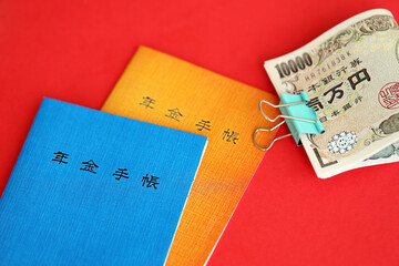 Japanese pension insurance booklets on table with yen money bills. Blue and orange books for japan pensioners close up