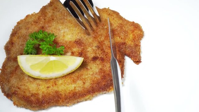 Cutting Wiener Schnitzel with fork and knife on a white background