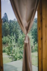 Selective focus of a green garden seen from a panoramic window with a beige curtain