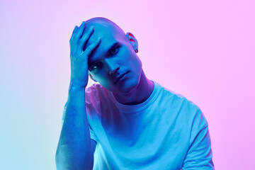 Portrait of young man with bald head, shaved face, inn casual t-shirt posing on gradient blue pink background in neon light. Concept of male beauty, body, youth, fitness, sport, health