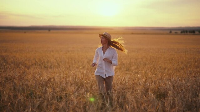 Romantic carefree happy woman running on yellow wheat field with spreading flying arms enjoying freedom calmness on rural nature during vacations holidays. Rest, relax in country, village outdoors.