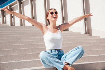 Beautiful smiling model in sunglasses. Female dressed in summer hipster white T-shirt and jeans....