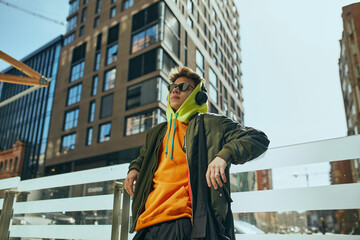 Young cool attitude man, student posing against urban, city views. model dressed trendy, neon...