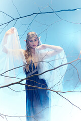 A young woman exudes fairy-like magic in a blue dress and white veil in a whimsical studio setting.