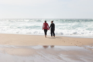 Two friends women Walking on a Beach Holding Hands