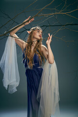 A young woman in a blue dress resembling an elf princess, delicately holds a branch in a studio setting.