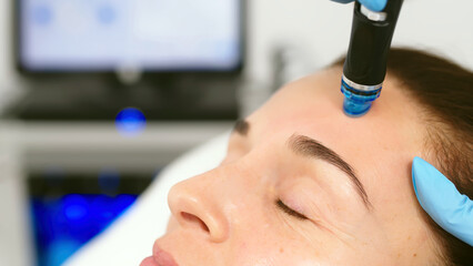 A cosmetologist performs vacuum cleaning and polishing of the facial skin of a middle-aged woman in...