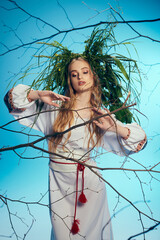 A young mavka in a white dress gently holds a tree branch in a magical and surreal studio setting.