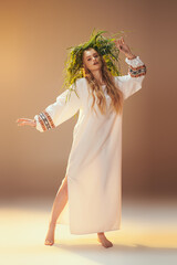 A young mavka in a white dress adorned with a green wreath, exuding an ethereal and mystical presence in a studio setting.