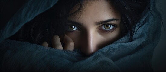 Woman with dark hair and blue eyes concealing beneath blanket - obrazy, fototapety, plakaty