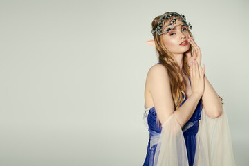 A young woman embodies an elf princess in a blue dress with a delicate veil in a whimsical studio setting.