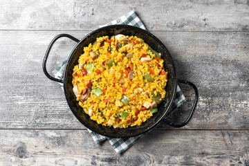 Yellow rice with chicken and vegetables on wooden table. Top view