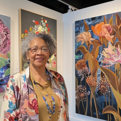 Senior artist standing beside her art showcasing in an art gallery.