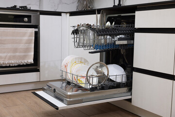 Open modern dishwasher with dirty tableware in kitchen