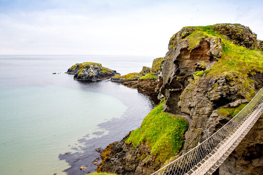 Fototapeta View from Carrick-a-Rede Rope Bridge, famous rope bridge near Ballintoy in County Antrim, Northern Ireland on Irish coastline. Tourist attraction, bridge to small island on cloudy day.