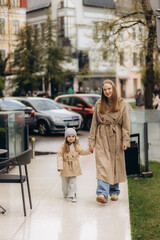 a young mother dressed in a coat walks with her daughter through the streets of the city
