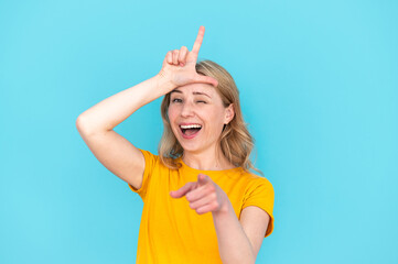 Smiling woman with finger on forehead showing loser gesture - obrazy, fototapety, plakaty
