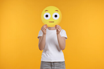 Woman covering face with surprised emoticon on yellow background