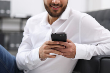 Young man using smartphone indoors, selective focus