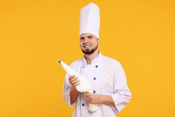 Happy professional confectioner in uniform holding piping bag on yellow background