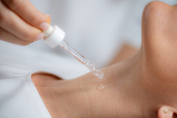 Cosmetician applies hyaluronic acid serum on woman's neck for targeted anti-aging benefits, enhancing skin elasticity and firmness