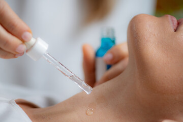 Cosmetician applies hyaluronic acid serum on woman's neck for targeted anti-aging benefits,...