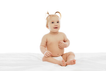 Happy little baby girl, toddler in diaper, with ponytails sitting and cheerfully smiling isolated on white background. Concept of childhood, care, health, well-being, parenthood