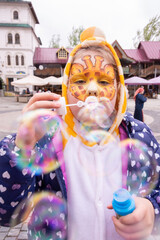 A girl is blowing soap bubbles on the street. A girl with a beautiful aquagrim on her face. Aquagrim.