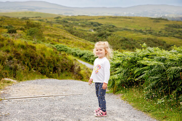 Cute little happy toddler girl running on nature path in Connemara national park in Ireland. Smiling and laughing baby child having fun spending family vacations in nature. Traveling with small kids