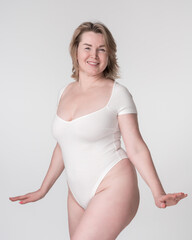 Portrait of happy plump mature adult blonde woman in white body suit posing in studio on white background. Healthy lifestyle, body care concept. Smiling plus size Caucasian model looking at camera