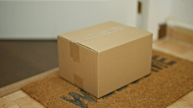 Cardboard package delivery at the doorstep inside a house with a welcome mat and red sneakers