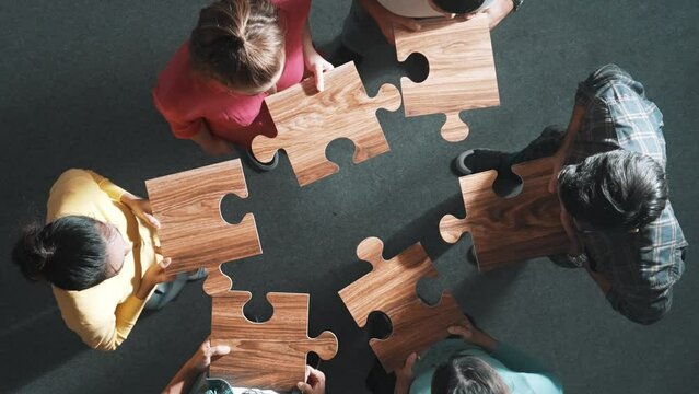 Top down view of business people gathering jigsaw together at meeting. Aerial view of diverse team collect or put piece of jigsaw puzzle together and standing while wearing casual cloth. Symposium.