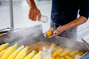 A street vendor roasts corn on a charcoal grill in Istanbul, Turkey. Misir, a popular Turkish street food, is freshly boiled or grilled sweet corn on the cob sprinkled with salt and spices. - obrazy, fototapety, plakaty