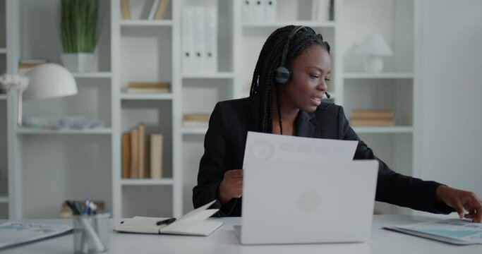Female office manager working on her laptop, sitting at desk, using headphones.