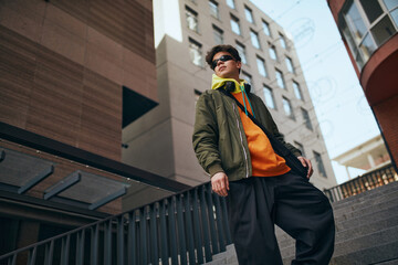 fashionable guy stands confidently against city skyline, his stylish outfit and sunglasses...
