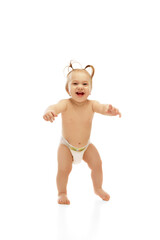 Full-length image of happy, smiling little baby girl in diaper cheerfully walking, playing and laughing on white background. First steps. Concept of childhood, care, health, well-being, parenthood