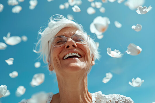 A joyful elderly woman smiles broadly, her face framed by floating white petals against a clear blue sky, epitomizing delight and freedom. hopecore concept