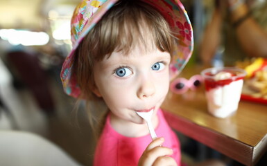 Satisfied little child licks spoon with ice cream on cafe background