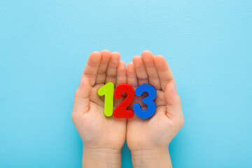 Baby boy hands holding and showing colorful 123 numbers on light blue table background. Pastel color. Time to learning. Closeup. Point of view shot. Top down view. - 783033191
