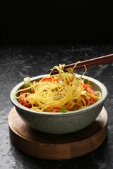 Stir-fry. Eating tasty noodles with meat and vegetables at dark textured table