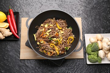 Stir-fry. Tasty noodles with vegetables, meat in wok and ingredients on dark textured table, flat lay