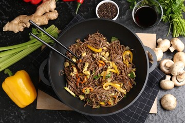 Stir-fry. Tasty noodles with meat and vegetables in wok served on dark textured table, flat lay