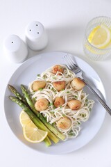 Delicious scallop pasta with asparagus, green onion and lemon served on white table, flat lay