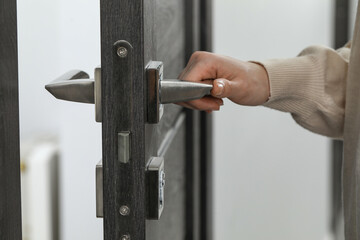 Woman opening wooden door indoors, closeup of hand on handle