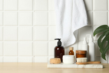 Different bath accessories and personal care products on wooden table near white tiled wall, space for text