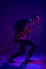 Talented jazz man, virtuoso playing saxophone in vibrant pink neon light against dark studio...