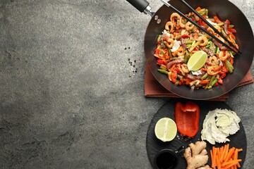 Shrimp stir fry with vegetables in wok and chopsticks on grey table, flat lay. Space for text